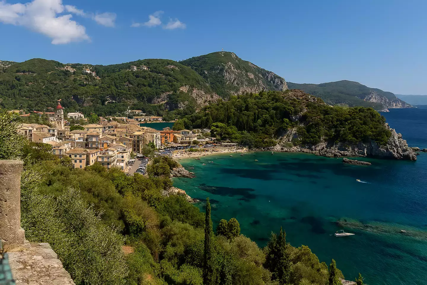 vue panoramique de Paleokastritsa en Grèce, avec ses criques turquoise, falaises verdoyantes, petits bateaux dans les baies, et le monastère perché sur la colline